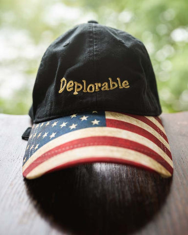 Show them how who you really are wearing this Deplorable Baseball Cap with "Deplorable" embroidered in gold color stitching. The hat's bill proudly displays an American Flag print. This hat has an adjustable fabric pull-through strap in the back. Available in Black. One size. 