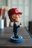 Donald Trump Bobble-Head / Desk accessory (Trump in a blue suit, red tie, and red MAGA hat.standing atop Presidential Seal with Make America Great Again around the foundation) side view