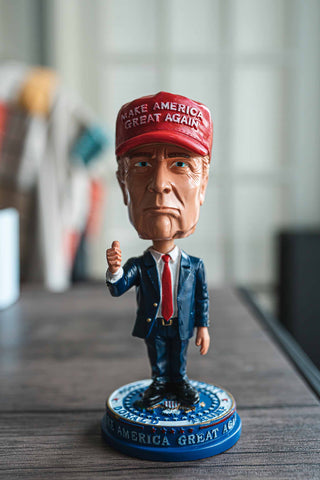 Donald Trump Bobble-Head / Desk accessory (Trump in a blue suit, red tie, and red MAGA hat.standing atop Presidential Seal with Make America Great Again around the foundation)