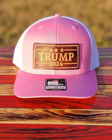 Trucker-Style Trump 2024 Leather Patch Hat with white mesh back.  The leather patch is custom made, hand-cut, and hand-stamped in the USA. Available in Pink. 