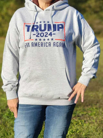 Stay warm and cozy in this Trump 2024 Fix America again hoodie sweatshirt with front pocket. Available in Light Heather Grey. Size M-XXXXL.