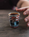 Trump Shot Glass - Trump Shot Glass.  Casual Trump pictured in a red MAGA hat, pointing, American flag design in the background.  One ounce.
